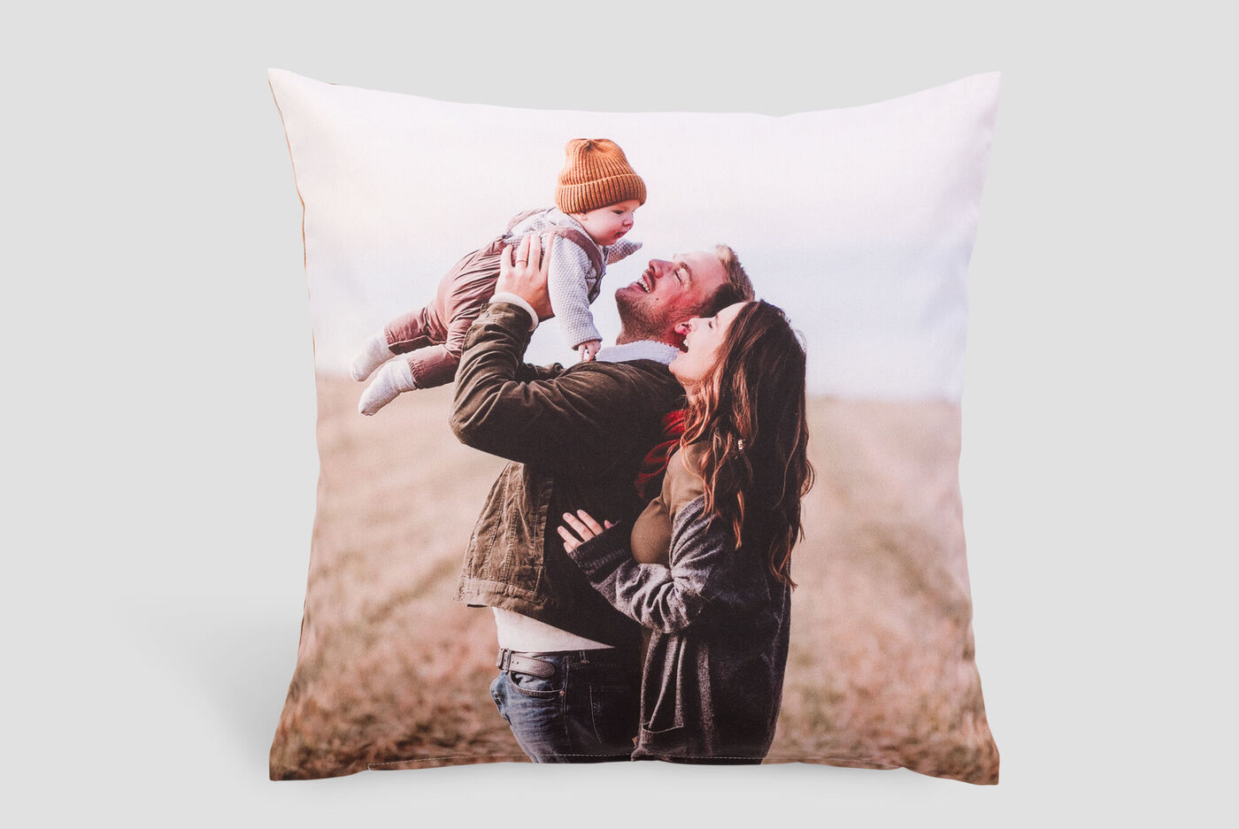 Une famille heureuse sur un coussin. Un père soulève son bébé, pendant que la mère sourit.